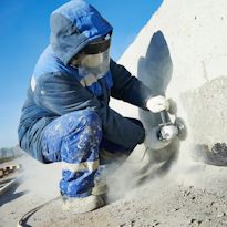 Worker wearing PPE and respirator while grinding on rock surface