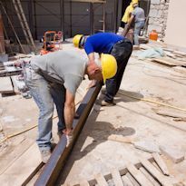 Three construction workers lifting heavy pipe on construction site
