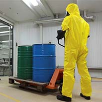 Employee wearing full-body personal protective equipment moving containers of hazardous chemicals