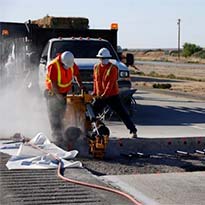 Two workers breaking up asphalt within work zone on road 