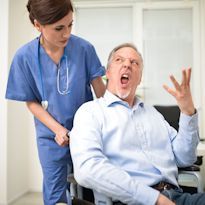 Healthcare worker moving upset patient in wheelchair