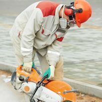 Construction worker wearing eye and face protection, and respiratory protecton while using circular saw